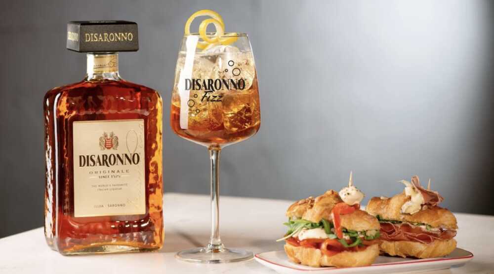 Bouteille d'amaretto Disaronno Originale avec un verre de Disaronno Fizz et deux sandwiches apéritifs